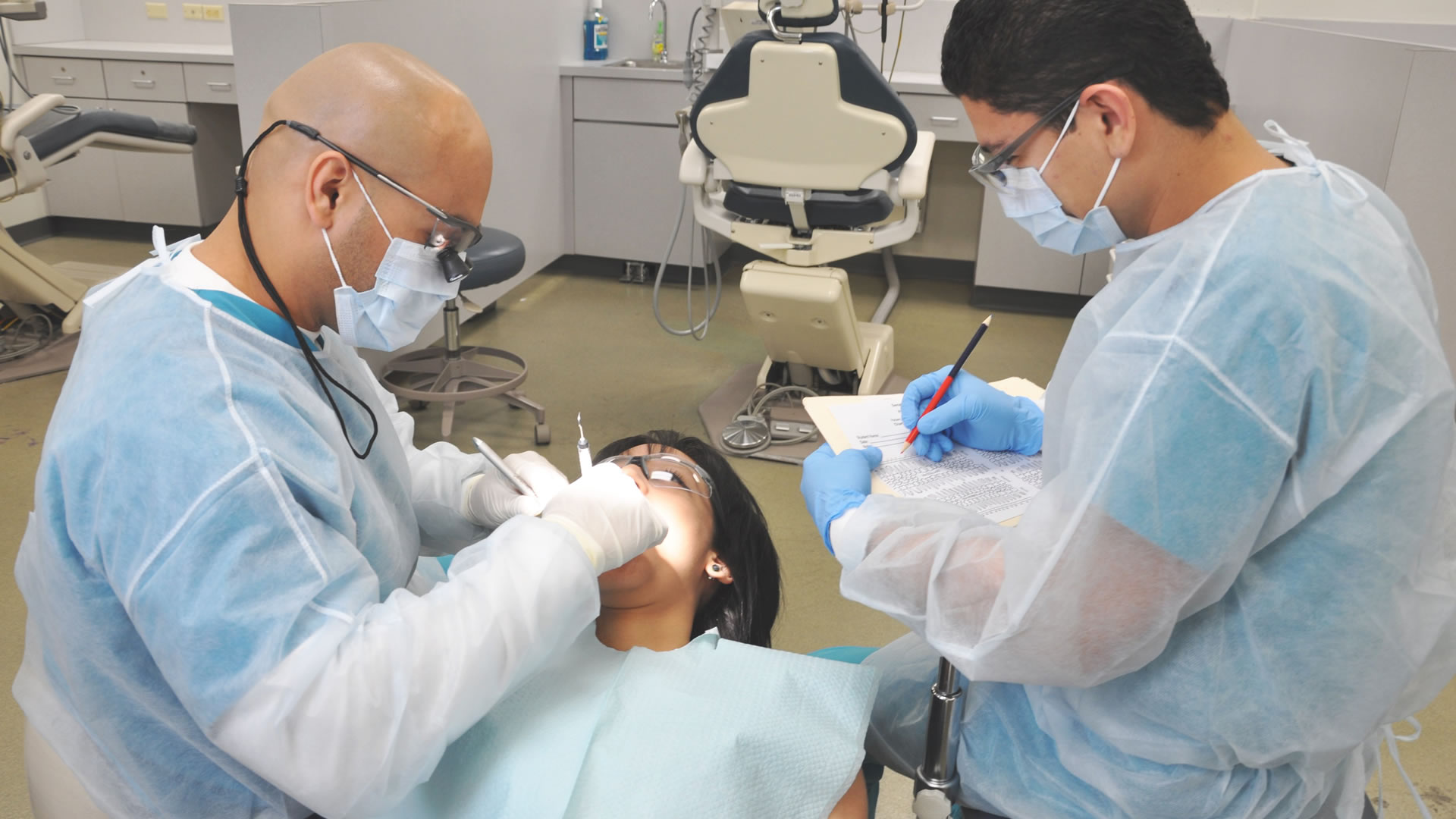 A student observes a dental hygienist working with a live patient 