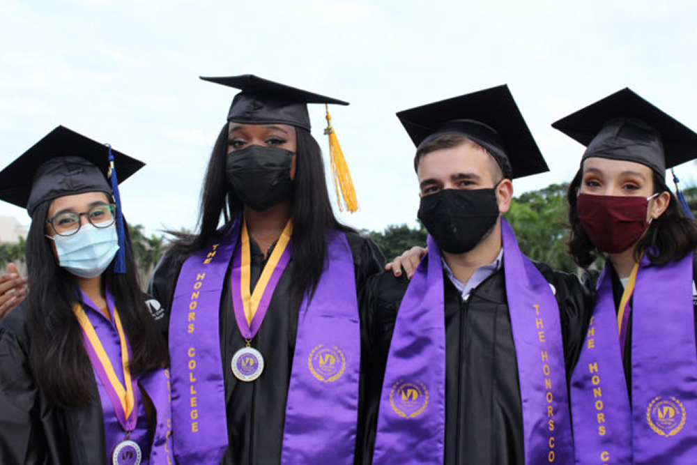 A group of Honors College graduates in their cap and gowns with masks celebrate their achievement