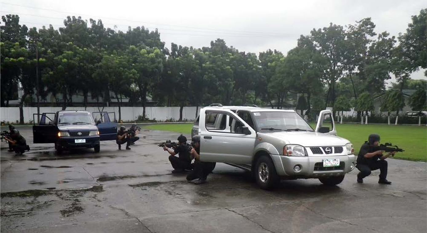 Several armed officers crouch by vehicles