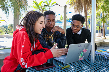 Three students hovering over a laptop