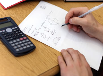 Picture of a student working on a math problem with the focus on his hands and the paper