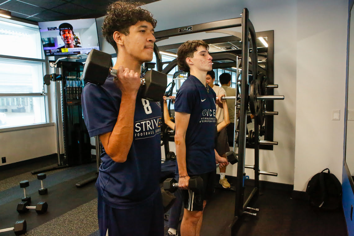 Two young men lifting dumbbells during a weight training session at the gym.