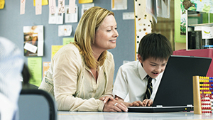 Teacher assisting a student on a PC