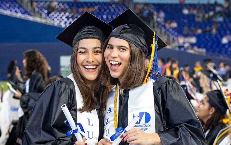 Two graduating students wearing their stole and holding their diplomas.
