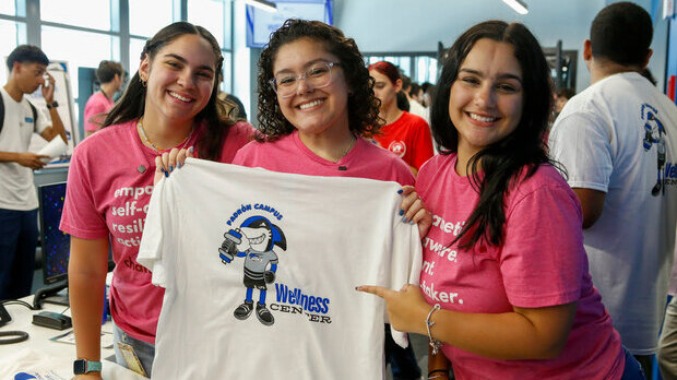 Three young women holding a Padrón Campus Wellness Center t-shirt.