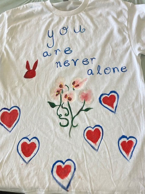 white tee shirt with the words 'you are never alone' hand painted on it