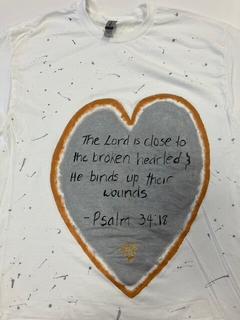 white tee shirt with the words 'the Lord is close to the broken hearted & he binds up their wounds, Psalm 34:18' hand painted on it